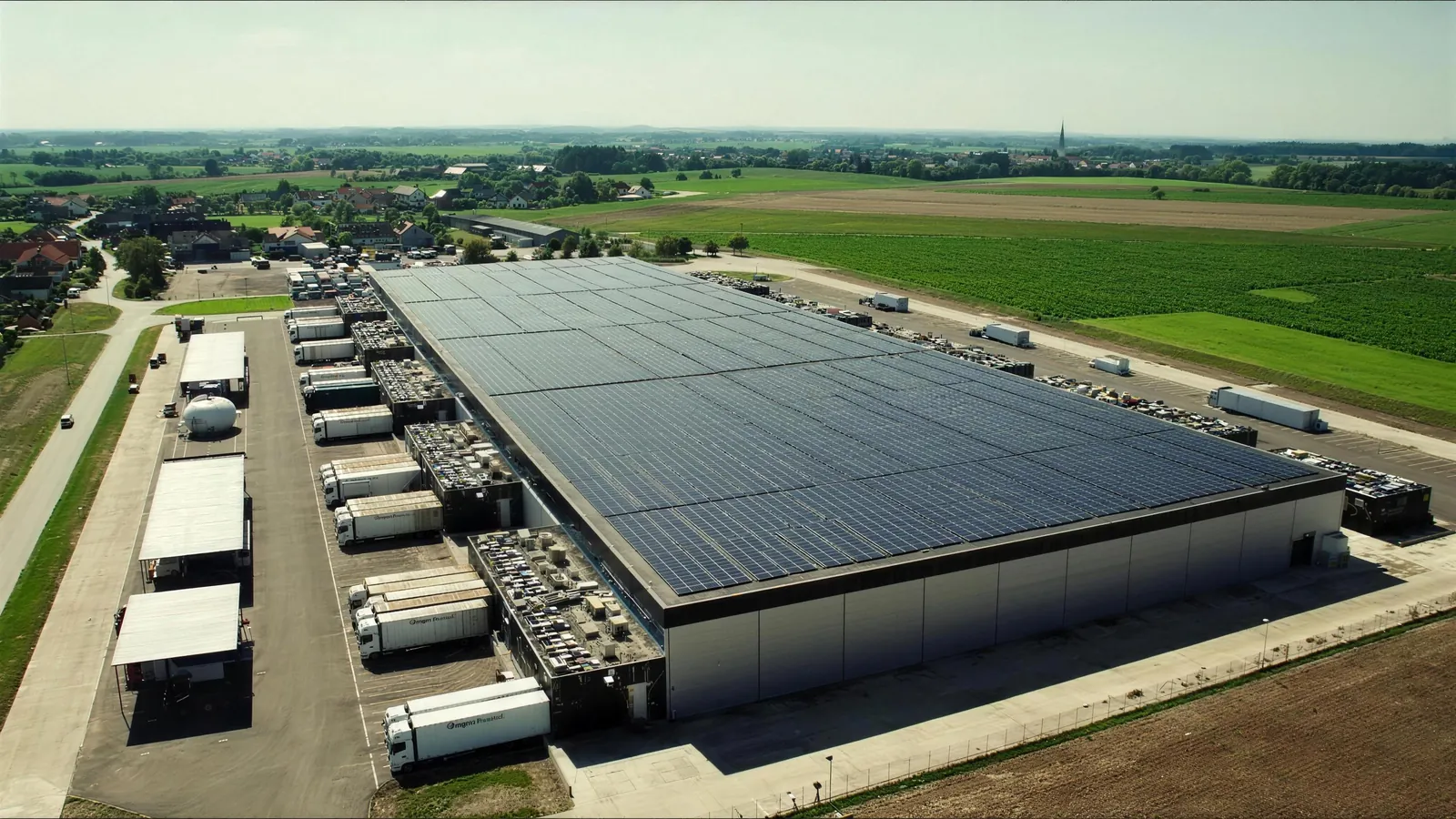 Luftbild eines Logistikzentrums mit Solardach, Lkw an den Toren und bayerischen Feldern