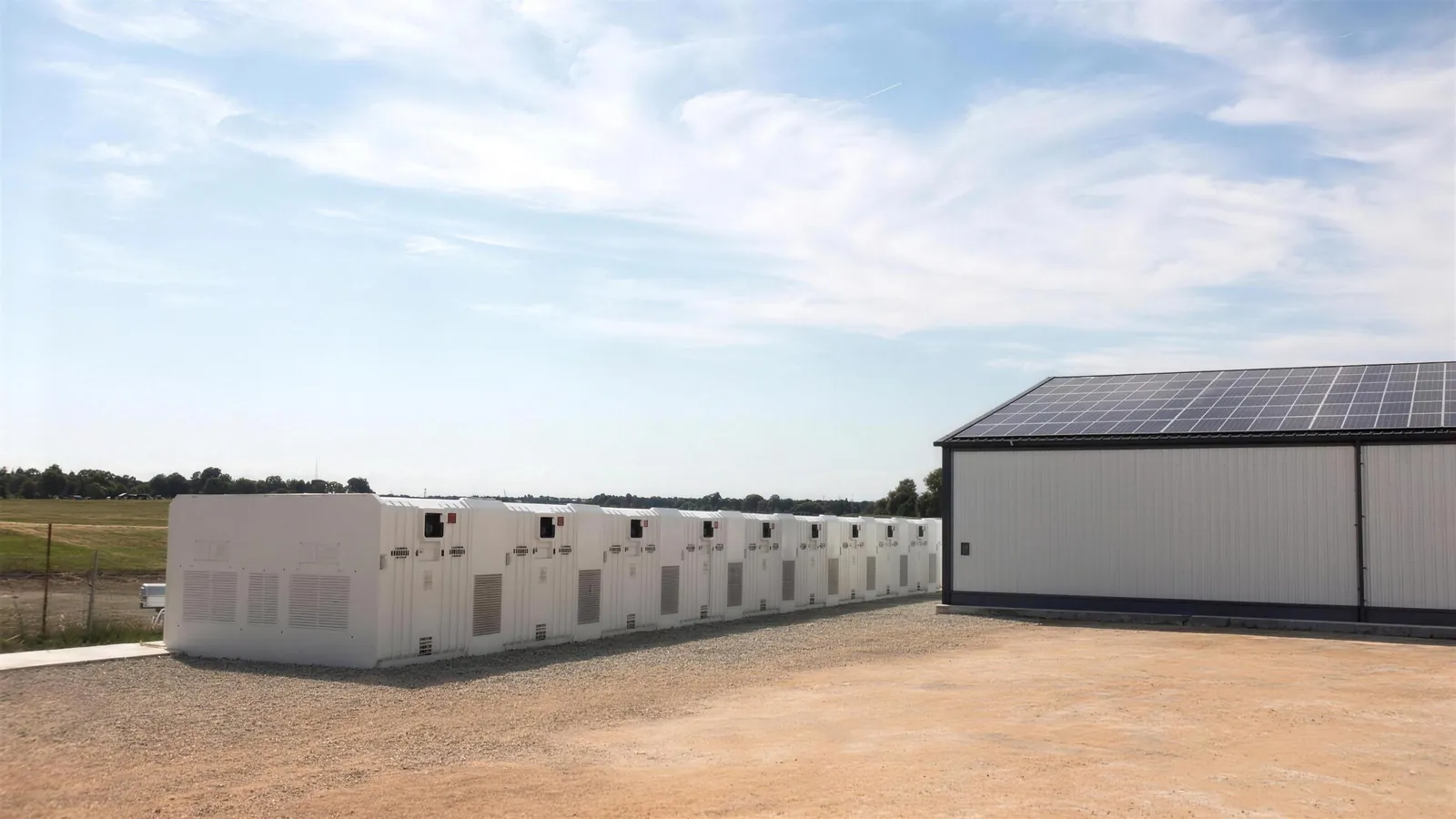 Weiße Batteriespeicher-Container neben einer Industriehalle mit Solardach